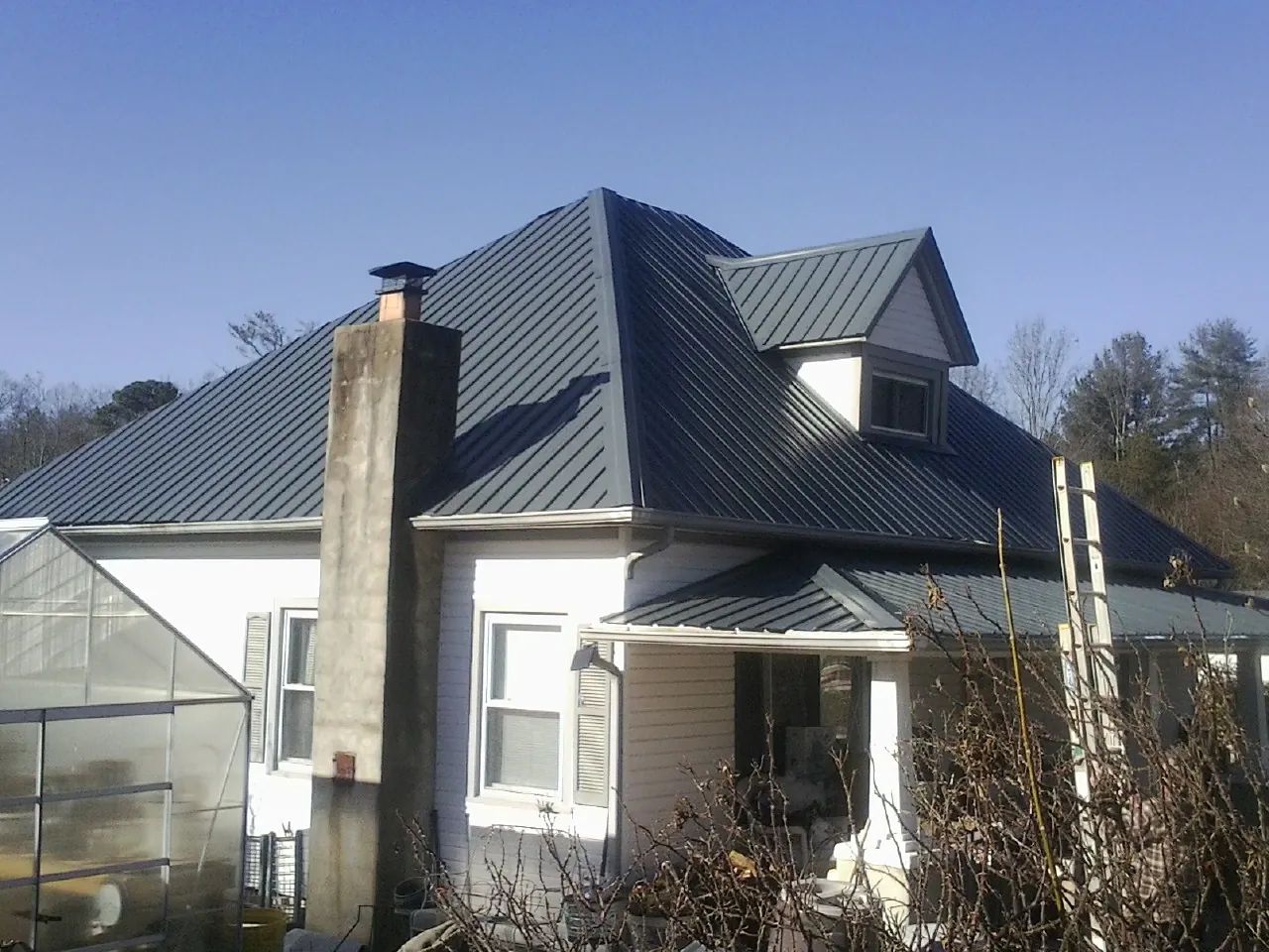 Dark blue standing seam metal roof on a white farmhouse with dormer — Slate & Tile Roof Repair by Roofing Brothers in Gilberton