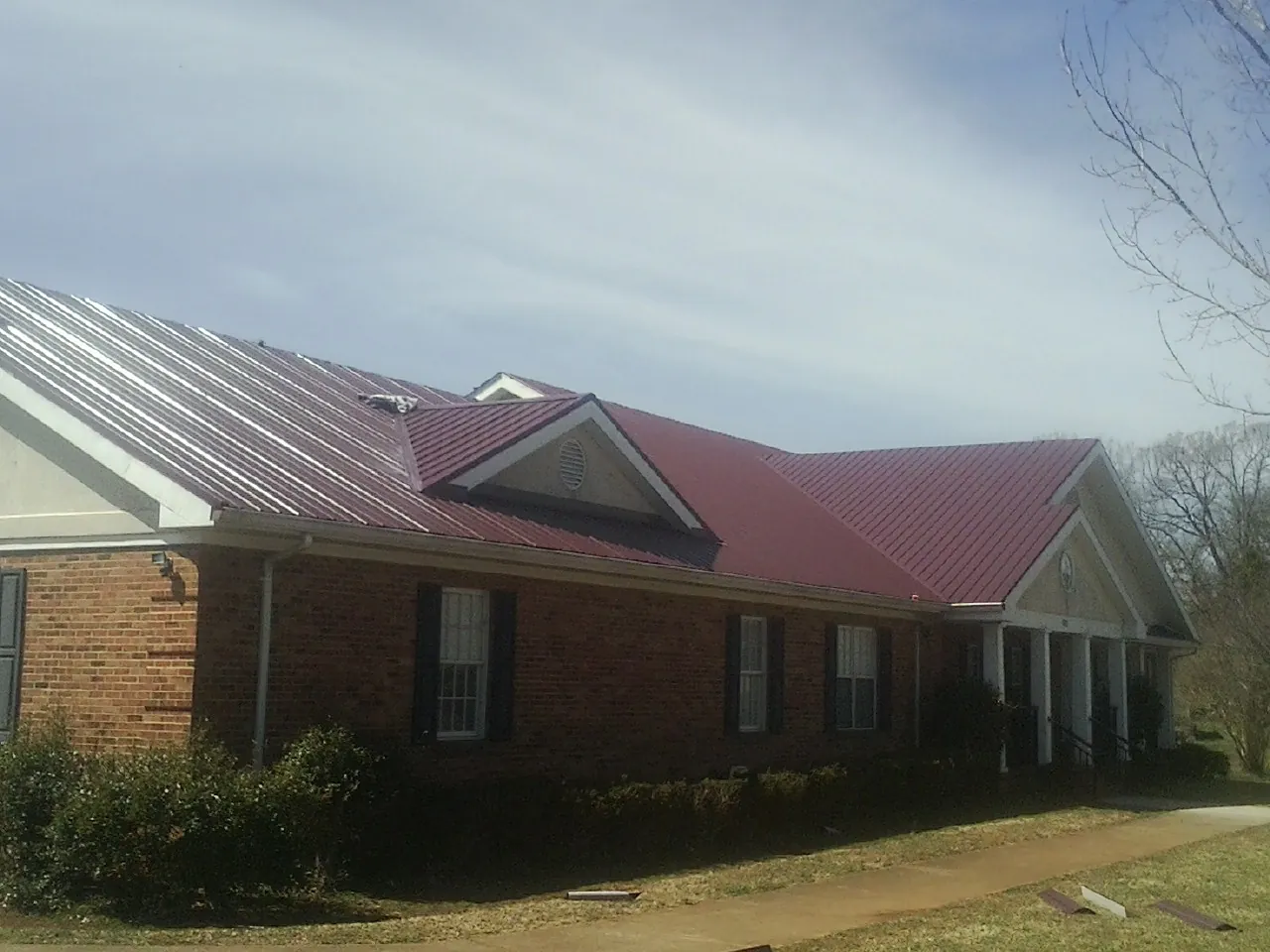 Red metal roof with gabled entries on a long brick building, from a Hail Damage Roof Repair job in Gilberton