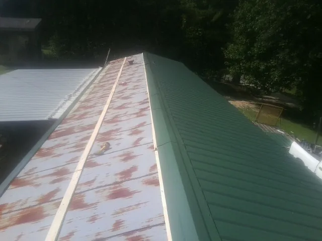 Old rusted panels beside newly installed green metal roofing — Wind Damage Roof Repair by Roofing Brothers in Gilberton