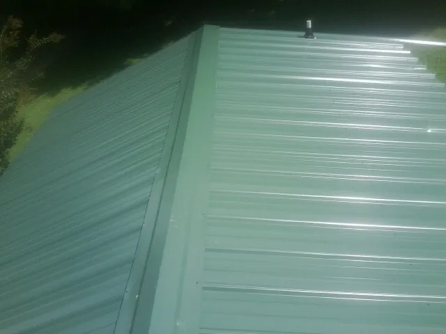 New green metal panels meeting at the ridge of a roof — Flat Roof Repair work by our crew in Gilberton
