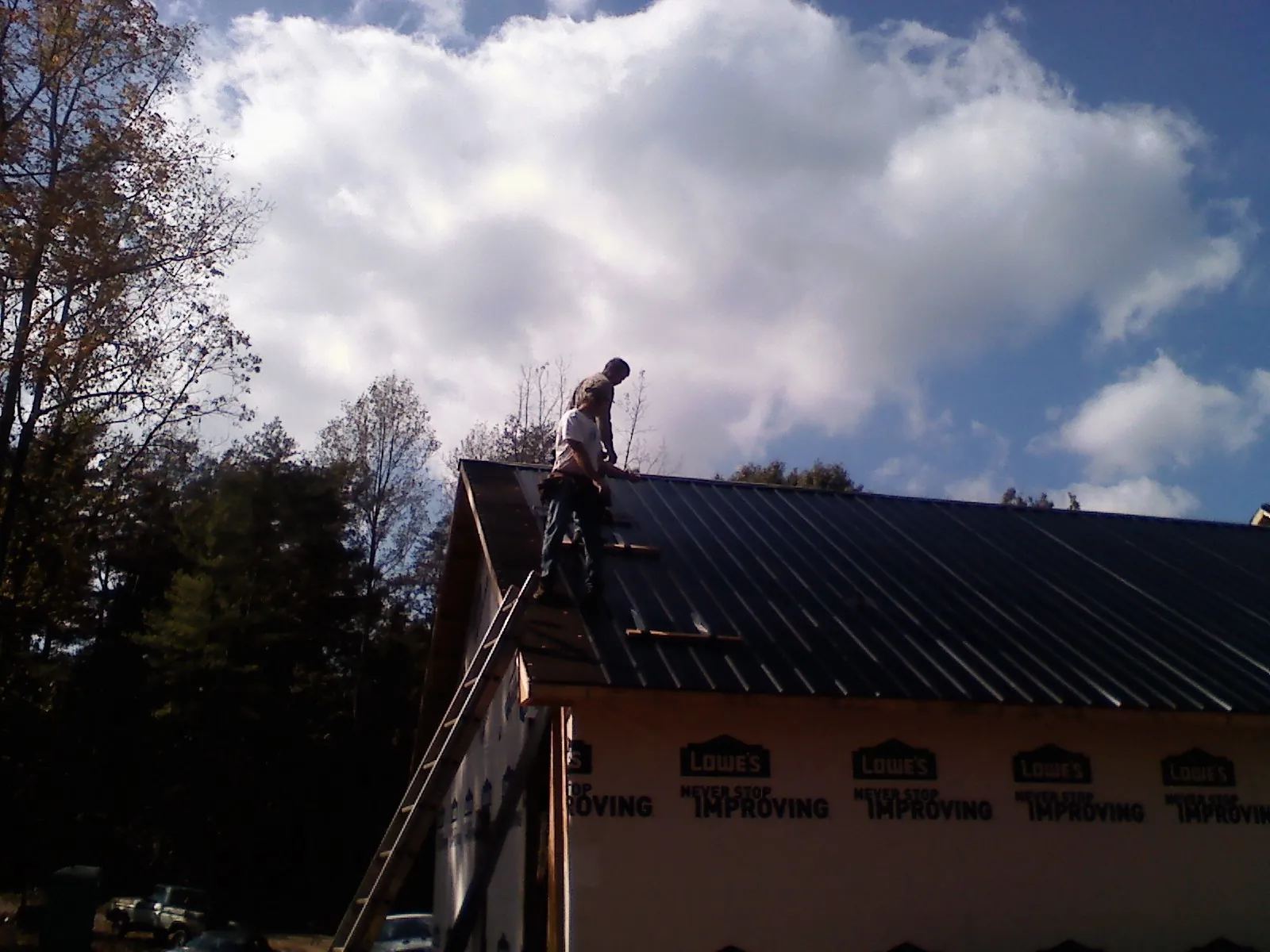 Roofer fastening dark metal panels high against a cloudy sky, from a Roof Inspection job in Gilberton