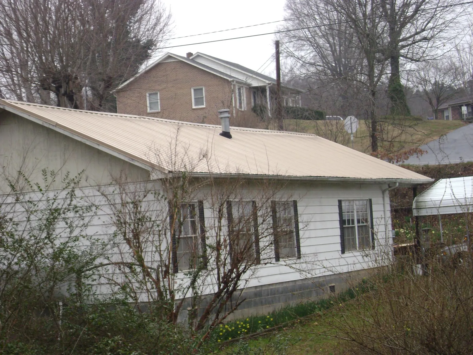 Tan metal roof on a white sided house set into a hillside — Commercial Roofing by Roofing Brothers in Gilberton