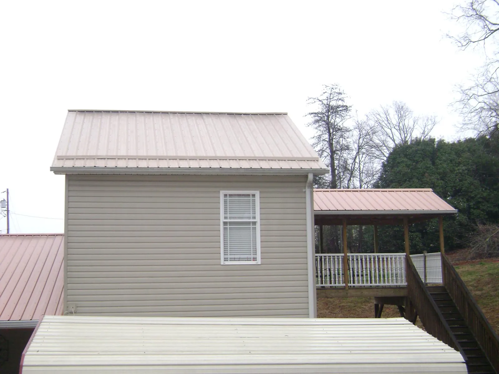 Tan metal roofs on a two story addition and attached porch, from a Roof Replacement job in Gilberton